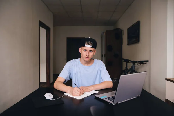 Un estudiante hace un trabajo de tarea mientras está sentado en su casa. Los adolescentes estudian en casa. Una mirada a la cámara . — Foto de Stock