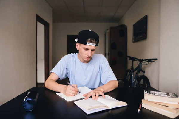 Estudiantes en casa. Él registra cuidadosamente las tareas y respuestas en su cuaderno. Tareas —  Fotos de Stock