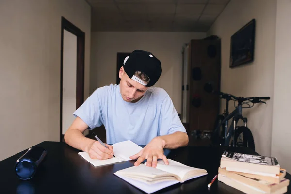 Studenten studieren zu Hause. Hausaufgaben. ein Teenager mit genauem Blick schreibt den Text in sein Notizbuch — Stockfoto