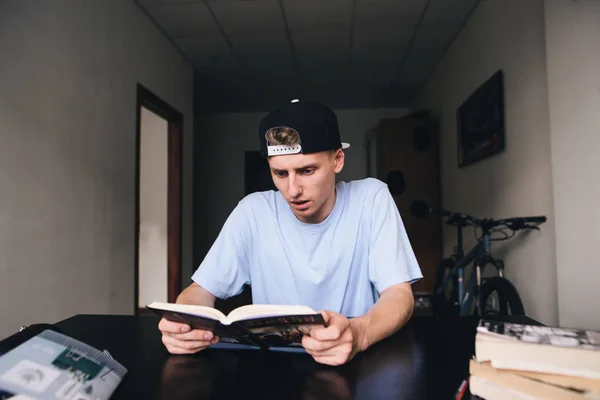 Σύλληψη νεαρού διαβάζει ένα ενδιαφέρον βιβλίο, στο σπίτι στο δωμάτιο. Διδασκαλία στο σπίτι. — Φωτογραφία Αρχείου
