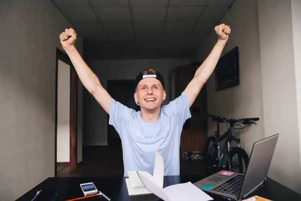 El estudiante está feliz porque ha cumplido todas las tareas. Adolescente levantó las manos hacia arriba Educar en casa su escritorio cerca de un ordenador portátil y libros . —  Fotos de Stock