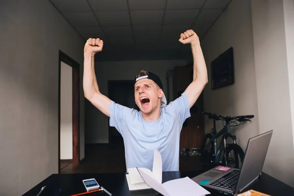 Hob der Teenager freudig die Hände. Unterricht zu Hause am Schreibtisch in der Nähe von Laptop und Büchern. — Stockfoto