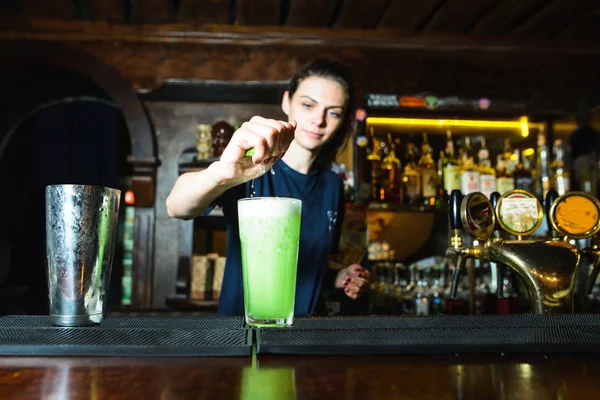 O fată barman creează un cocktail verde frumos într-un club de noapte. Barmanul stoarce sucul de lămâie într-un cocktail alcoolic . — Fotografie, imagine de stoc