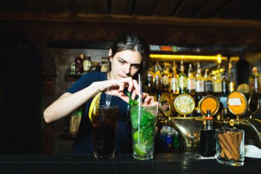 Bir kadın barmen bir alkollü kokteyl barda oluşturur. Barmen nane kokteyller süsle. Parlak alkollü içecek.