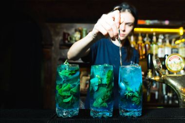 Barmen parlak alkollü kokteyl malzemeleri karıştırır. Kız barmen güzel bir mavi içki barda yapar..
