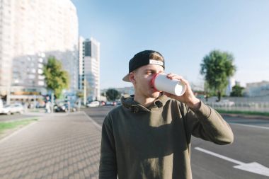Bir öğrenci şehir etrafında bir yürüyüş için sıcak bir içki içer. Genç adam sokak arka plan üzerinde duruyor ve kahve içiyor. Yaşam tarzı ve insanlar kavramı.
