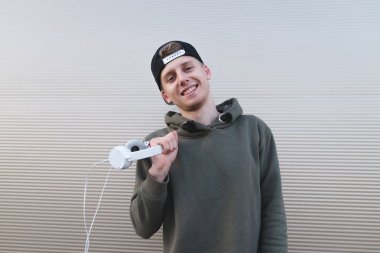 Olumlu bir genç adam, hafif bir duvara yakın duruyor kulaklık ve gülümsüyor tutar.