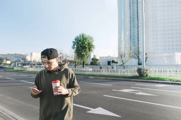 Bir fincan kahve onun elinde olan genç bir adam onun telefon şehirde yürüyüş sırasında bir ileti yazar. Yollar ve binaların arka plan üzerinde. Yaşam tarzı ve insanlar kavramı.