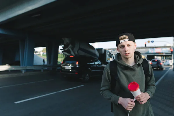 Een knappe man met koffie handen tegen de achterkant van de weg en auto's onder de brug staan en kijken naar de camera — Stockfoto