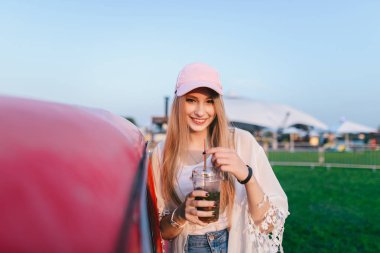 Elleri soğuk bir içecek ile bir araba yakın duran ve gülümseyen güzel bir genç kız portresi. Yaz tatili.