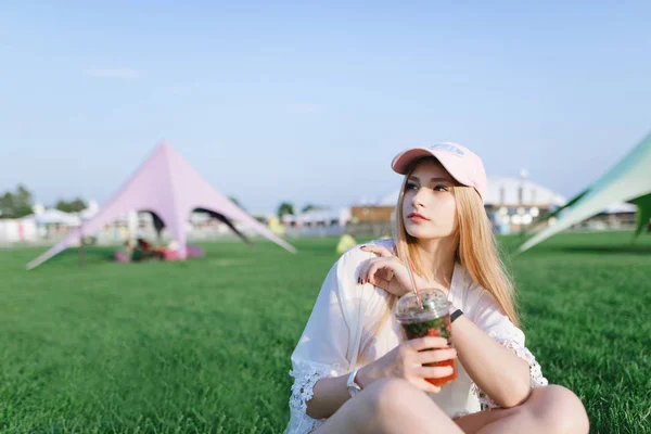 Retrato de uma menina bonita elegante com uma limonada em seus braços descansando no gramado no parque e olhando para o lado — Fotografia de Stock