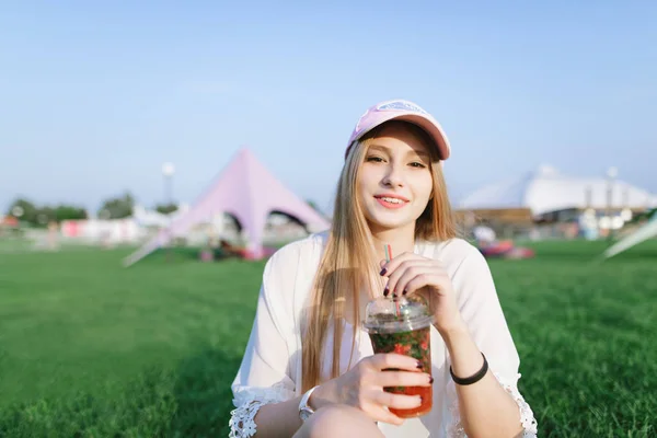Retrato de uma linda menina sorridente com uma bebida refrescante em seus braços descansando no parque. Conceito de verão . — Fotografia de Stock