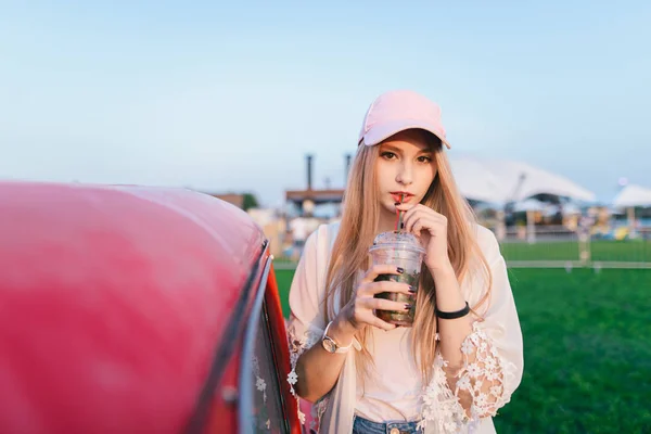 Menina elegante e bonita bebe um coquetel em um parque de recreação perto de um carro vermelho. Conceito de verão . — Fotografia de Stock