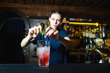 Barmen kız güzel serin kırmızı barda kokteyl oluşturur. Barmen bir alkollü kokteyl limon suyu sıkar.
