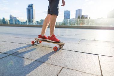 Güneş zemin karşı kaldırımda bir longboard üzerinde binen bir kaykay bacaklar. Sokak kavramı.