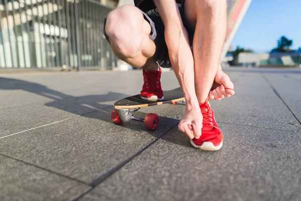 Un pattinatore uomo in località di scarpe da ginnastica rosse da terra cavalcando su un longboard. Concetto stradale . — Foto Stock