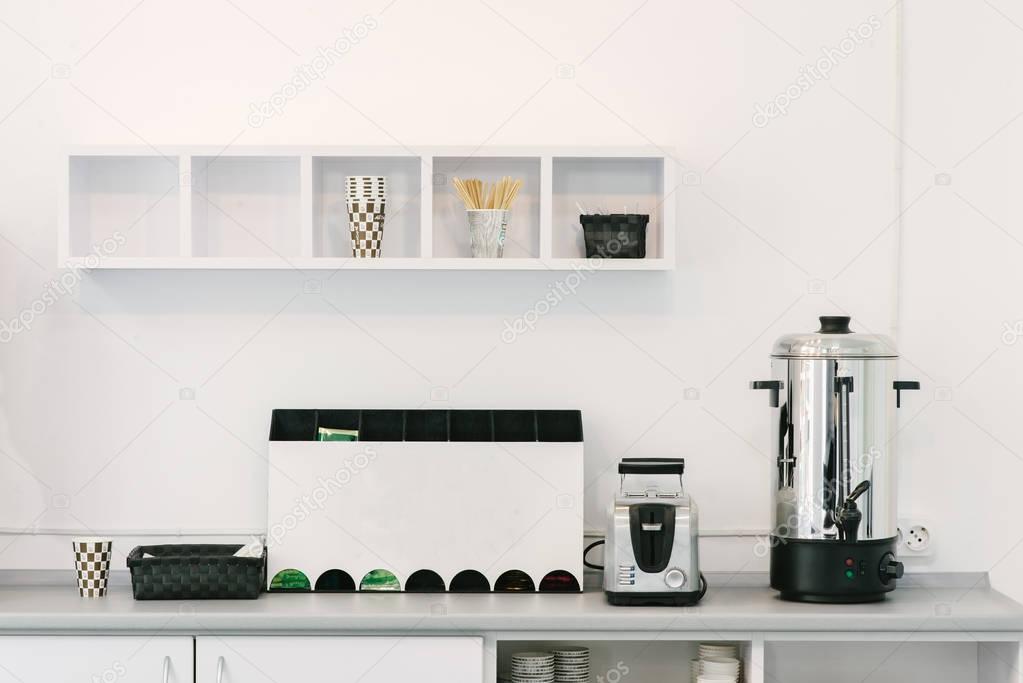 Modern minimalist design of the kitchen. Household appliances on the kitchen table in the office. Office kitchen.
