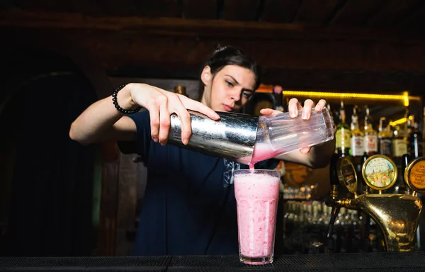 La barista ragazza crea un bel cocktail alcolico rosa. Il barman versa gli ingredienti dallo shaker in un bicchiere — Foto Stock