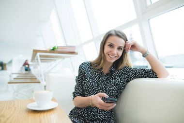 Gülümseyen güzel kadın bir şık modern kafede oturur ve bir maraton kullanır. Kahve molası. İş kadını iş arasında bir kopma.