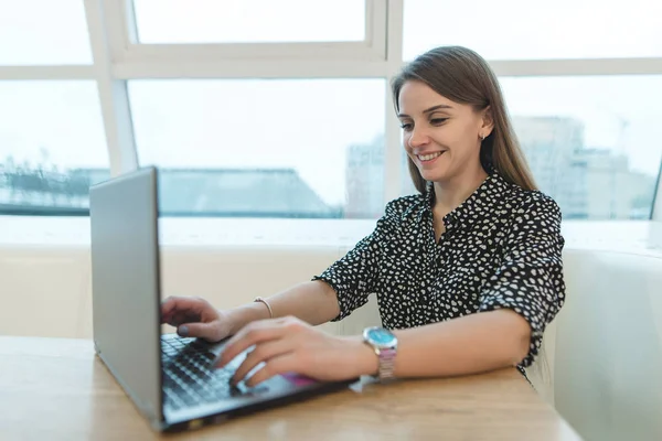 Gülümseyen bir iş kadını bir kafede oturur ve bir dizüstü bilgisayar kullanarak. Bir kafede otururken klavye metin yazarak iş kadını.