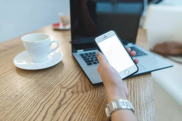 Tangan wanita dengan telepon di tangan terhadap laptop dan latar belakang kopi. Konsep bisnis. Wanita bisnis di kafe . — Stok Foto