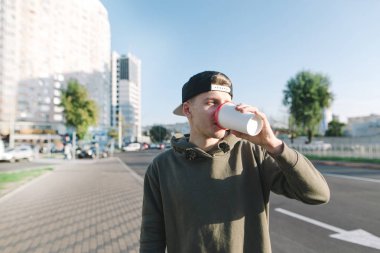 Bir öğrenci şehir etrafında bir yürüyüş için sıcak bir içki içer. Genç adam sokak arka plan üzerinde duruyor ve kahve içiyor. Yaşam tarzı ve insanlar kavramı.
