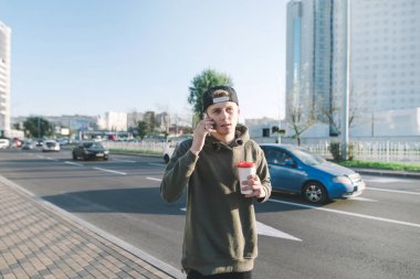 Bir fincan ile şehir gezen ve telefonda konuşurken şık genç bir öğrenci. Arabalı yolun karşı. Yaşam tarzı ve insanlar kavramı.