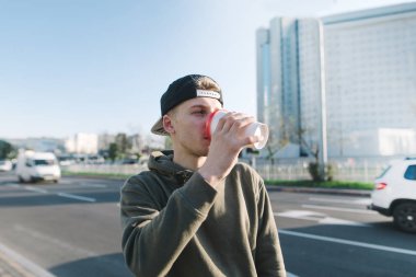 Bir öğrenci şehir etrafında bir yürüyüş için sıcak bir içki içer. Genç adam sokak arka plan üzerinde duruyor ve kahve içiyor. Yaşam tarzı ve insanlar kavramı.