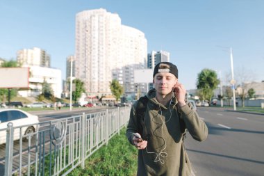 Yakışıklı bir delikanlı bir sırt çantası ve kulakları kulaklık ile müzik şehir etrafında yürürken hoşlanır. Caddenin arka plan üzerinde. Yaşam tarzı ve insanlar kavramı.