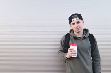 Bir sırt çantası ve bir fincan kahve bir ışık duvar arka planı elinde bir gülümseyen genç erkekle.
