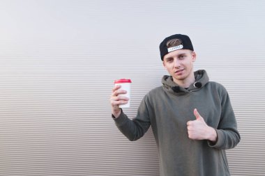 Yakışıklı bir genç adam onun elinde kahve ile bir başparmak hafif bir arka plan üzerinde göstermek yukarıya