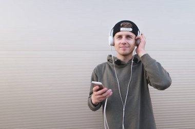 Gülümseyen genç biri kulaklık müzik dinler ve açık renkli bir akıllı telefon tutar.