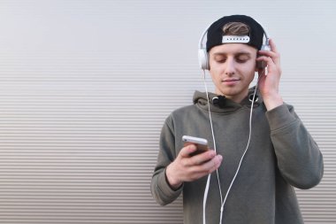 Elleri ve kulaklık kafasına bir telefon ile duvar arka plan üzerinde duran bir adam portresi. Genç bir adam müzik keyfi.