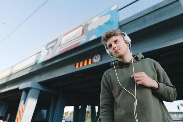 Straat portret van een jonge man die luisteren naar muziek in de koptelefoon op de achtergrond van de brug. — Stockfoto