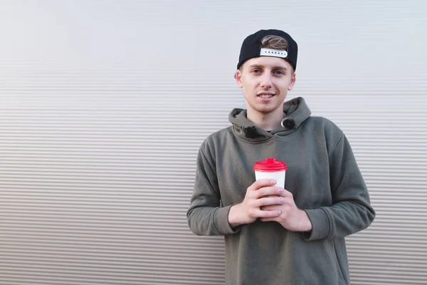 Portrait d'une jeune étudiante élégante coiffée d'une casquette sur un fond clair avec une tasse de boisson chaude dans les mains . — Photo