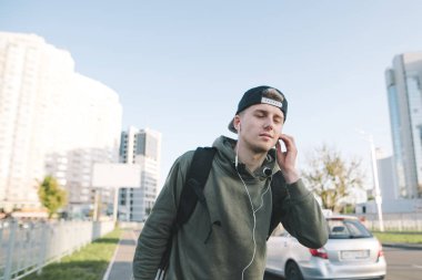 Sokakta yürürken ve kulaklık oynamak müzik keyfi bir şirin ve şık genç adam. Üzerinde arka plan şehir ve arabalar. Yaşam tarzı