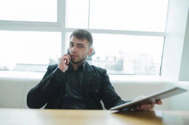 Elinde bir tablet ile bir öğrenci kameraya bakar ve kafede öğle yemeği saatinde telefonda konuşuyor. Kahve molası ile becerikli alet. Şık modern kafe.