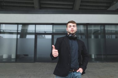 Güzel bir adam bir takım elbise ve sakallı bir başparmak modern mimari arka plan üzerinde gösterir. İş gibi. Adam takdir