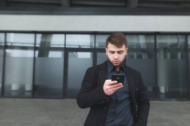 Arka planı karanlık bir bulanık duvar onun smartphone dikkatle bakar bir genç işadamı sakal ve bir ceket ile sokak portresi.