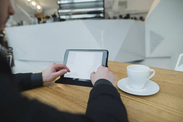 Un uomo usa internet con un tablet seduto in un caffè per una tazza di caffè. Lo studente utilizza un tablet in un caffè luminoso ed elegante . — Foto Stock