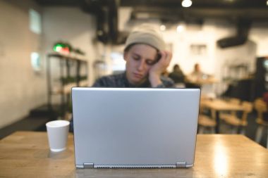 Uykulu bir çevirmen bir rahat kafe ve bir dizüstü bilgisayar için çalışıyor oturuyor. Bir dizüstü bilgisayar ile bir kafede hipsters. Dizüstü bilgisayarda odaklanmak.
