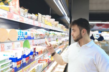 Bir sakallı bir adam satın gıda bir süpermarkette. Genç bir adam süpermarket raflarında süt ürünleri seçer.