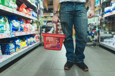 Bacakları ve kırmızı bir alışveriş çantası bir süpermarkette malları satın alan bir adam. Ürünleri piyasada seçin. Mağazada alışveriş.