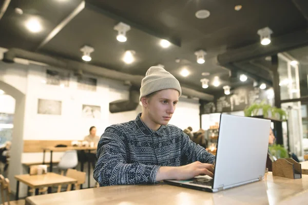 Un joven freelancer trabaja para un portátil en un acogedor café. El estudiante usará internet en el café . —  Fotos de Stock