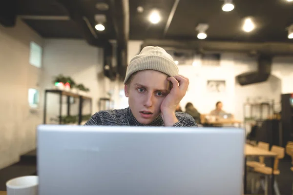 Задуманный молодой человек смотрит на монитор своего ноутбука в уютном кафе за чашкой кофе. Фрилансер работает в кафе. . — стоковое фото