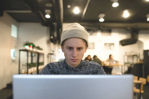El freelancer trabaja para un portátil en un acogedor café. Un joven marido hipster usa una computadora en un café para una taza de café . — Foto de Stock