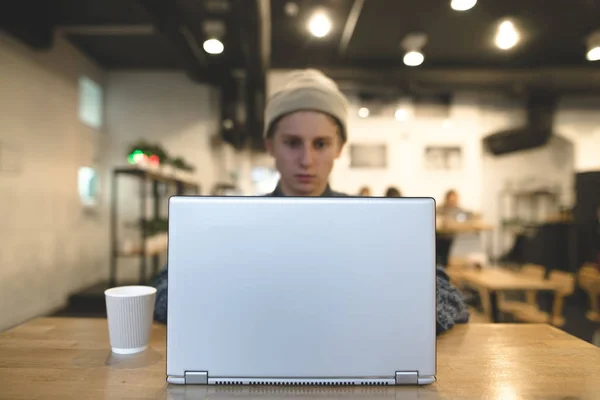 El freelancer trabaja para un portátil en un acogedor café. Un estudiante usa una computadora portátil en un café. Concéntrate en el portátil . —  Fotos de Stock