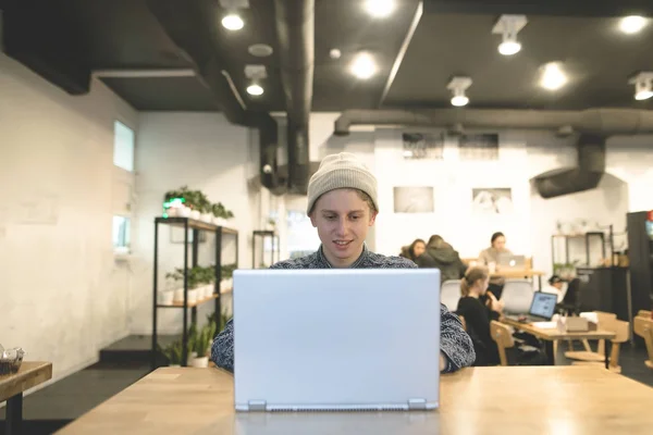 Положительный студент наслаждается ноутбуком в уютном кафе. Стильные хипстеры работают за компьютером в кафе . — стоковое фото