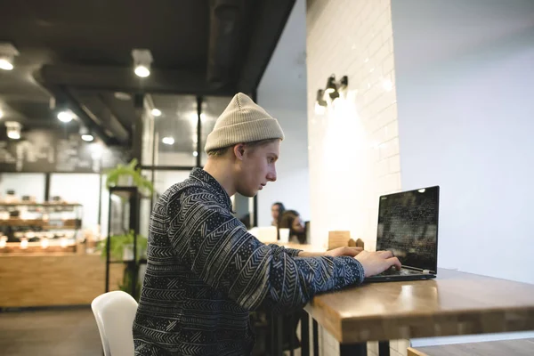 El freelancer trabaja para un portátil en un acogedor café. Un estudiante sentado en un café en la mesa y usando una computadora portátil. Trabajo en Internet . —  Fotos de Stock