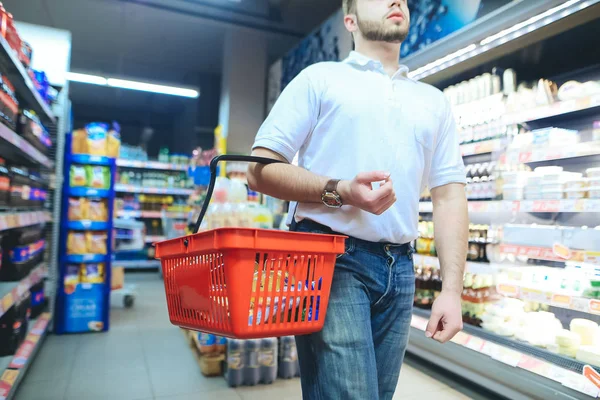 Un hombre con una cesta roja pasea por el supermercado. Un hombre compra bienes en un supermercado . — Foto de Stock